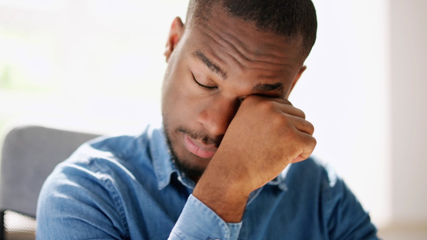 A young African man with a worried expression, sitting at a desk in front of a computer.