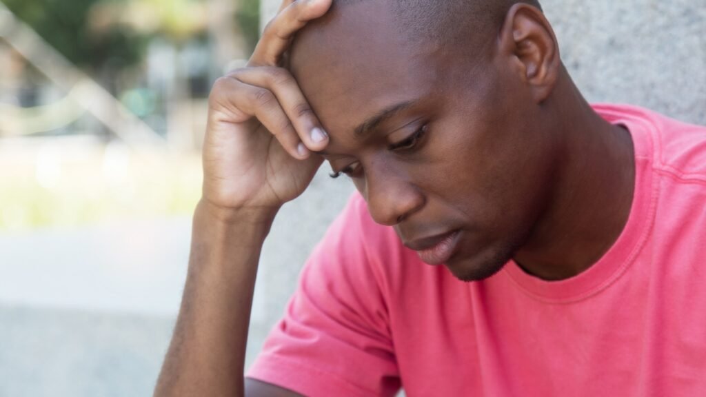 A man sitting, with his hand on his forehead.